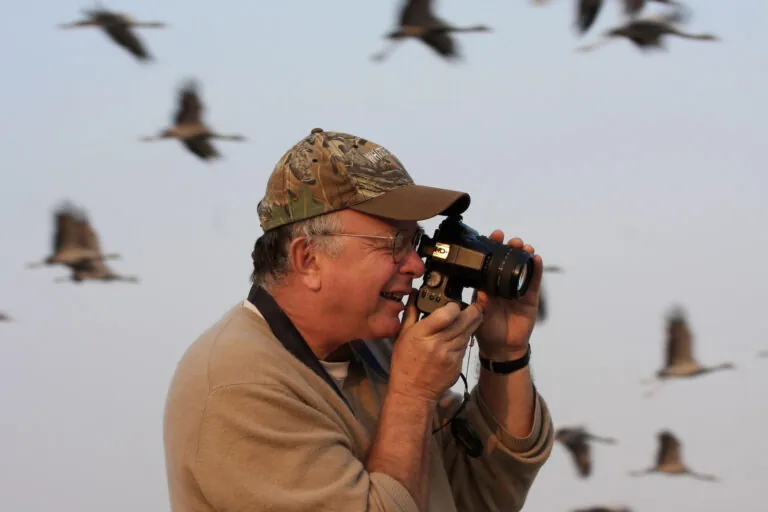 George Archibald taking photos with cranes flying in background