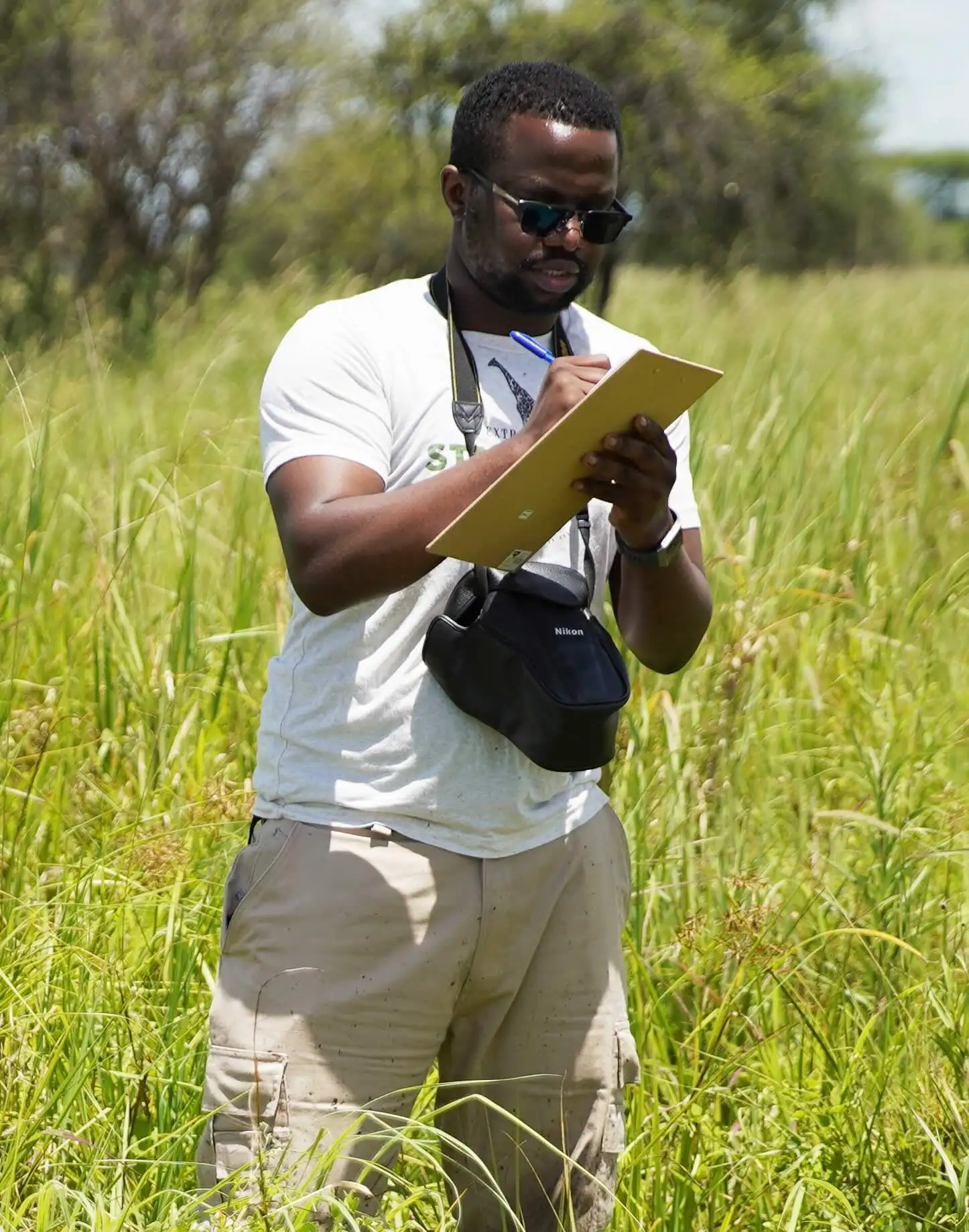 Arthur Muneza in field of grass with camera and notepad